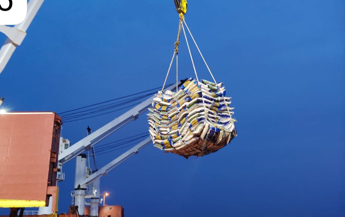 Ship’s crane lifting a sling of bagged rice against a clear sky